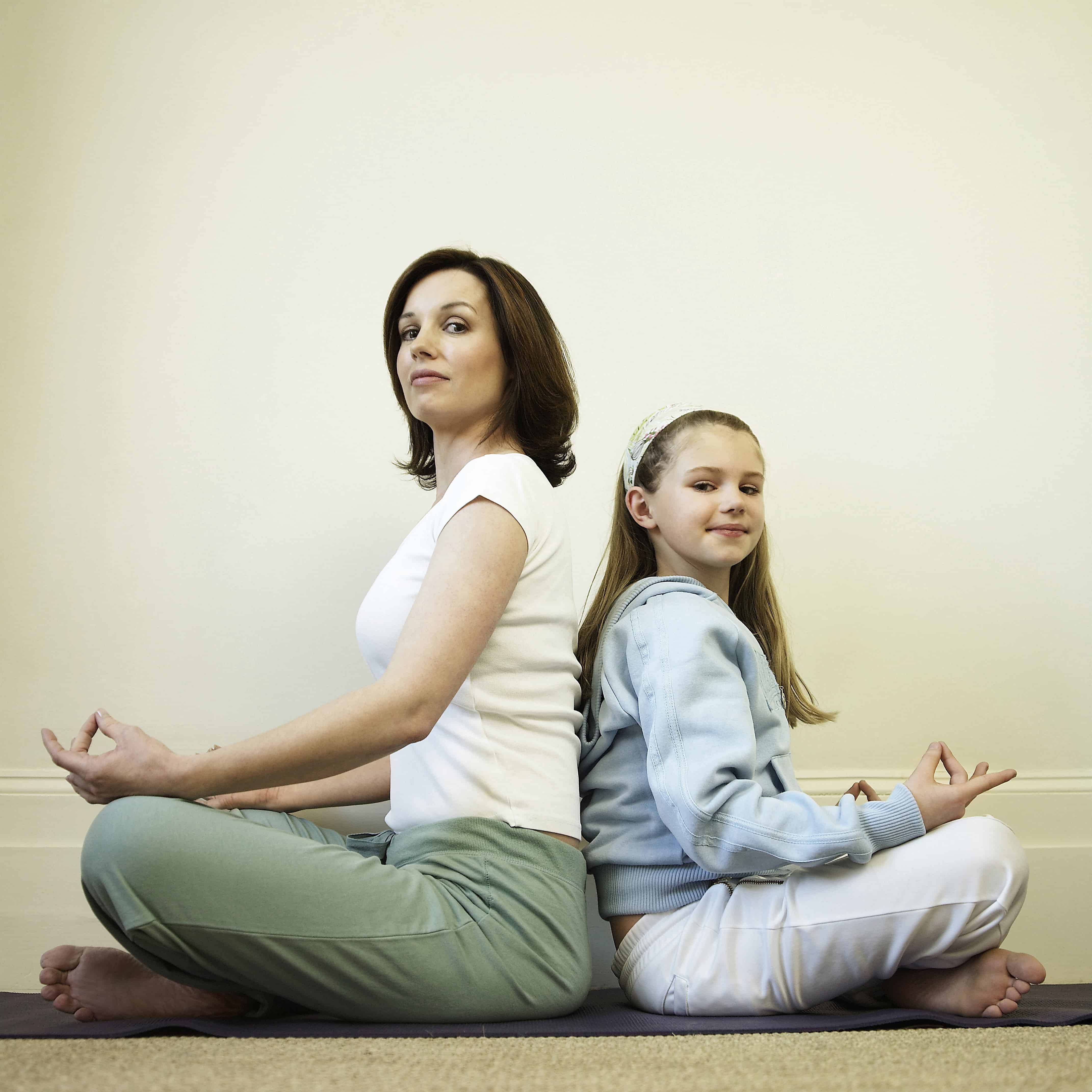 Mother and daughter sitting in lotus pose back-to-back