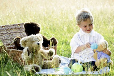 Happy little boy sitting in a field having a picnic with teddy bears