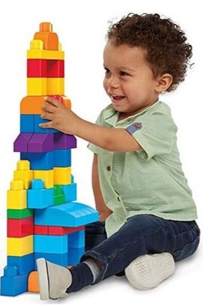Little boy smiling and playing with large Mega-Bloks tower