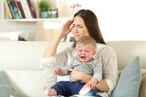 overwhelmed mom with crying toddler in her lap