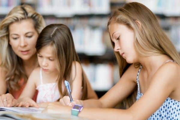 One homeschool child working while mom explains concept to other child