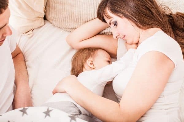 Woman laying in bed with her breastfeeding infant cuddling.
