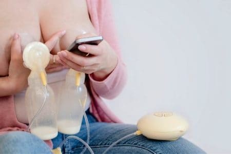 woman using double breast pump and looking at phone
