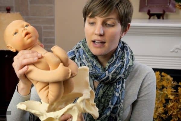 Maura from Mama Natural Birth Course holds a baby doll above a model of pelvic bones to show how the baby can go through during breech birth.
