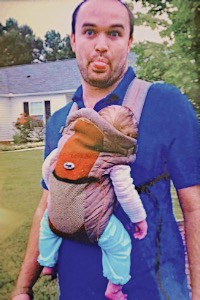 Man wearing baby in soft structured carrier that doesn't support baby's hips
