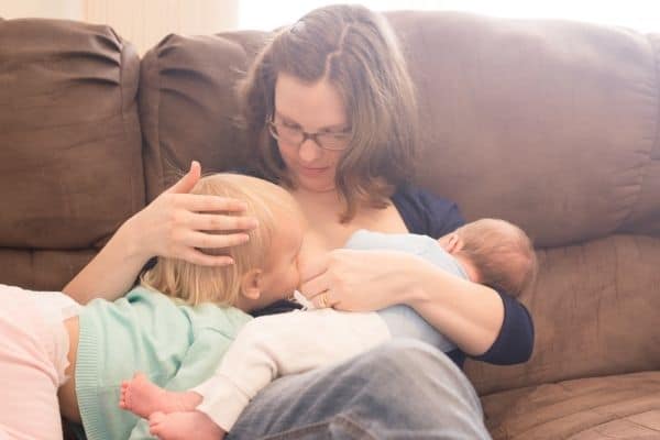 mother tandem nursing newborn son and toddler daughter