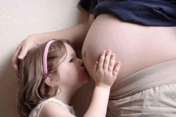 Toddler girl kissing her mother's pregnant belly