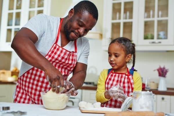 Little girl and daddy wearing matching gingham aprons and kneading dough
