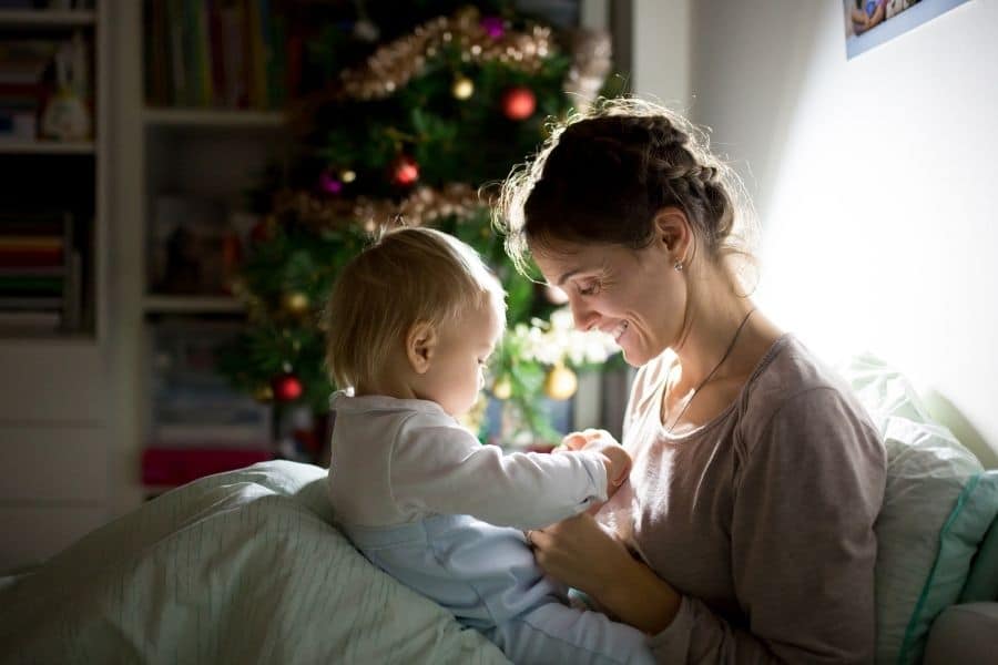 Mother and baby cuddled up in bed with Christmas tree in background
