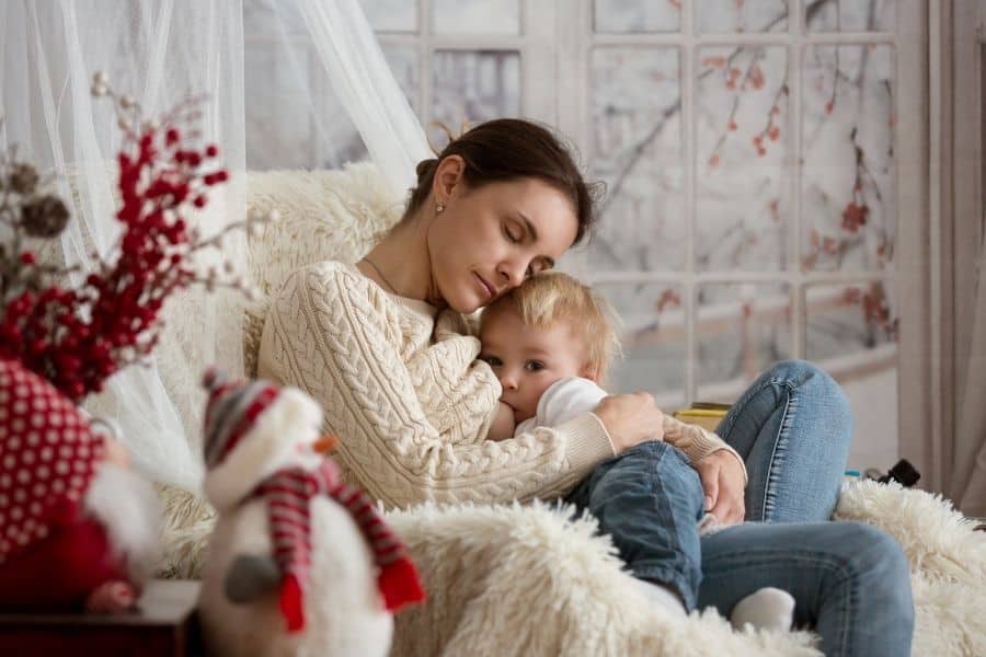 toddler cuddled up in mother's lap breastfeeding in front of holiday scene