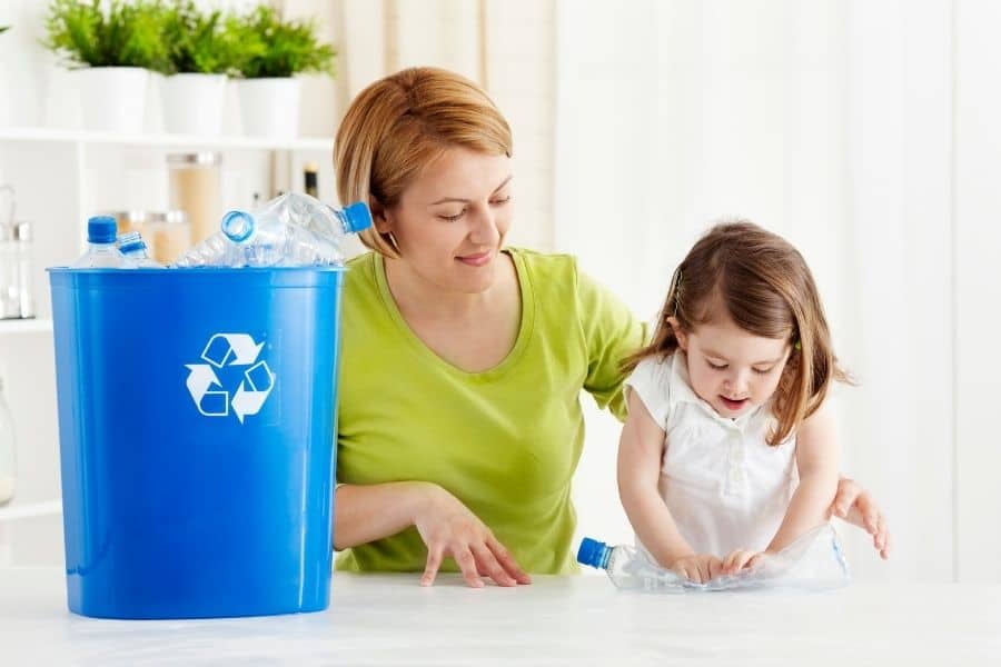 mother helping preschooler crush plastic bottles for recycling