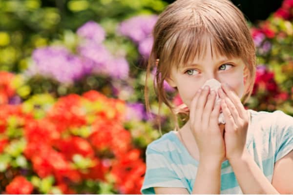 Little girl blowing her nose by the flowers.