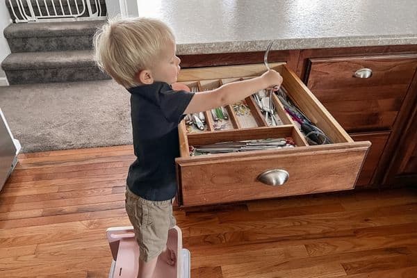 toddler using Little Partners 3-in-1 booster seat to do chores of putting away forks from dishwasher