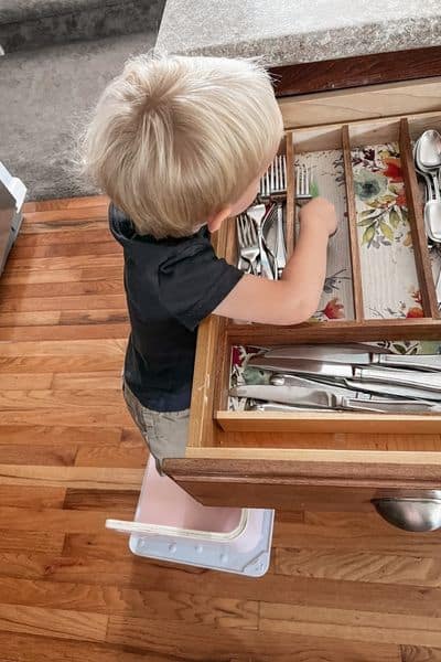 2 year old boy using Little Partners 3-in-1 Learning Booster seat as step stool to put away forks in drawer