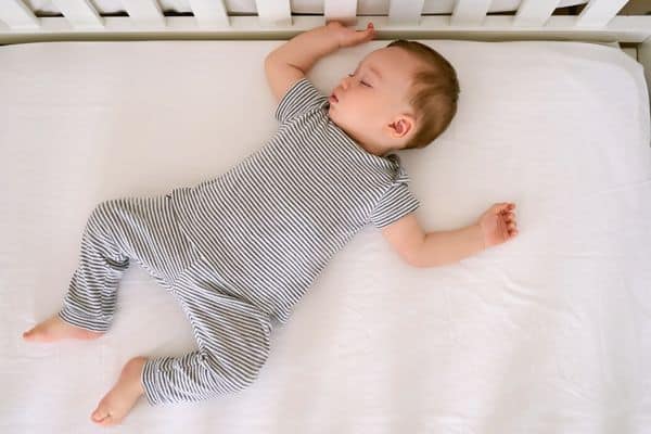 Baby sleeping in crib with firm mattress, no toys, blankets, or pillows with them.