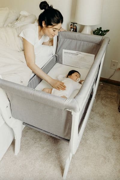 Shnuggle Convertible Air Bedside sleeper bassinet with baby in it. The non-toxic co sleeper is strapped safely beside the mother's mattress.