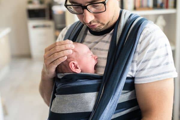 Man with yawning baby wrapped in baby carrier