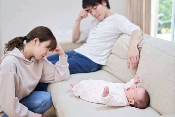baby lying on sofa crying while mother and father look on frustrated