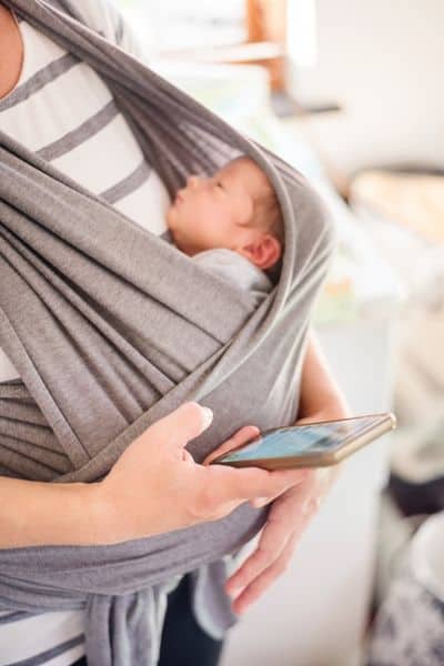 Woman looking at phone while wearing newborn
