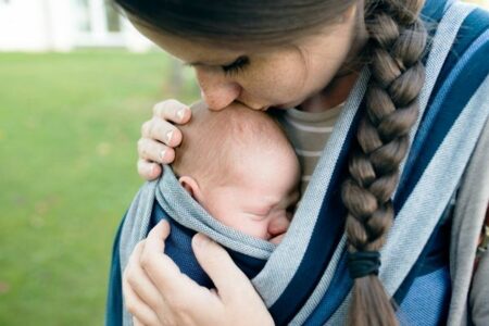 A woman kissing a newborn baby's forehead that's in a carrier attached to her