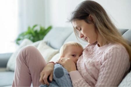 Woman sitting on couch while breastfeeding her baby
